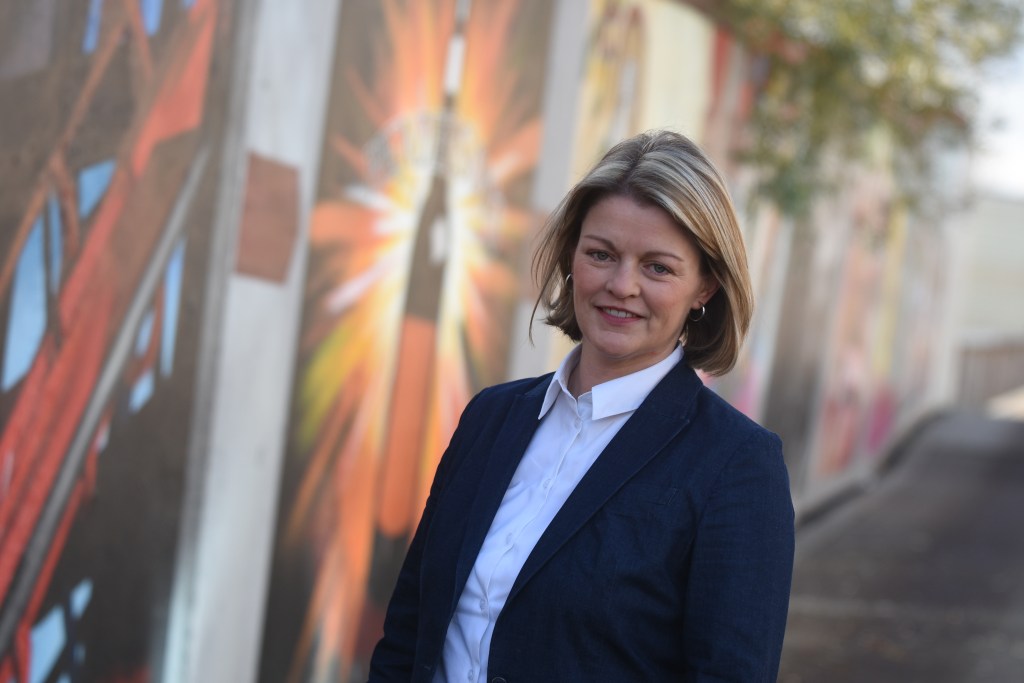 Profile picture of Kerry Leng wearing a white shirt and dark jacket standing in front of a colourful mural.